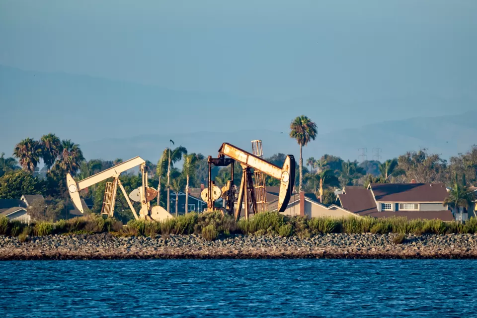 Oil drilling pumps on a wetland beach in California with houses in background
